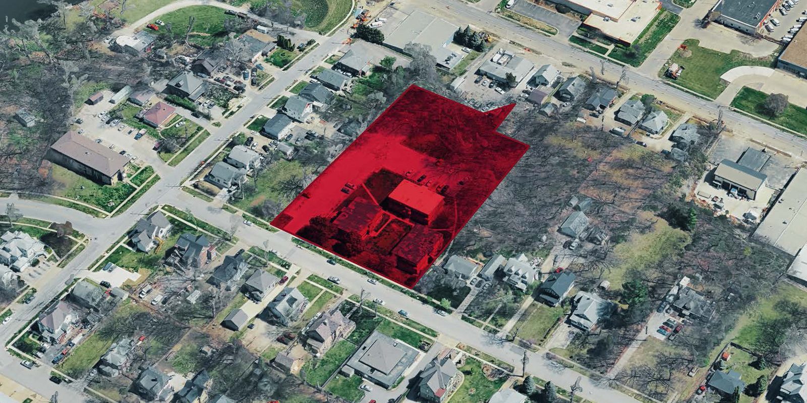 Aerial view of a suburban neighborhood with a red overlay highlighting a specific property. The area is surrounded by residential houses, roads, and some commercial buildings. Trees and greenery are visible throughout the neighborhood.