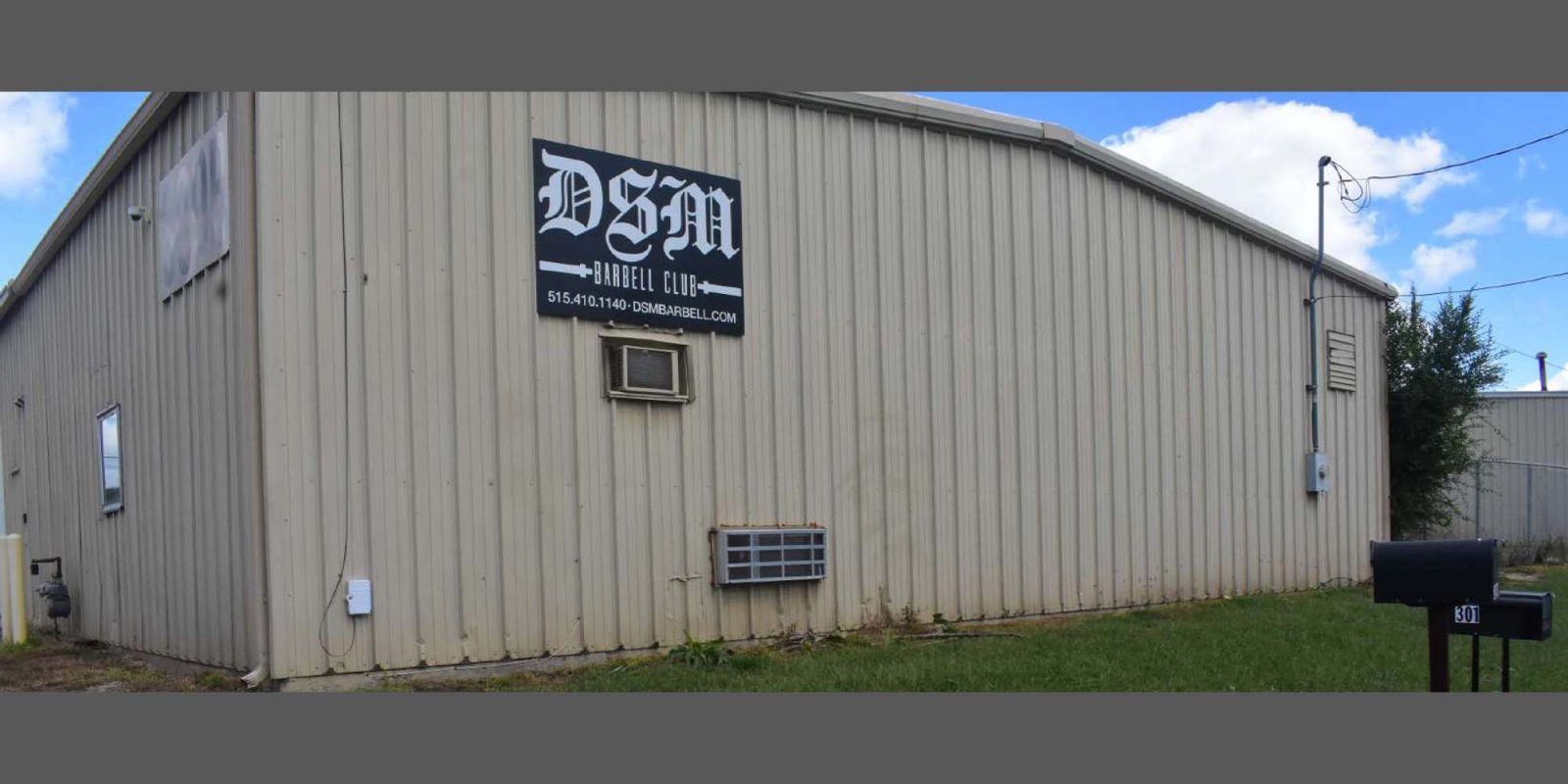 A beige metal building with a sign reading "DSM Angel Club" and an email address on the side wall. There is an air conditioning unit, a grassy area, and a black mailbox labeled "4131" in front.